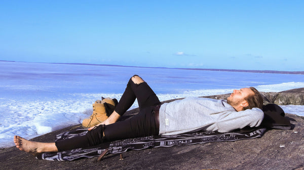mies makaa paljaalla kalliolla keskellä järven jäätä ottaen aurinkoa